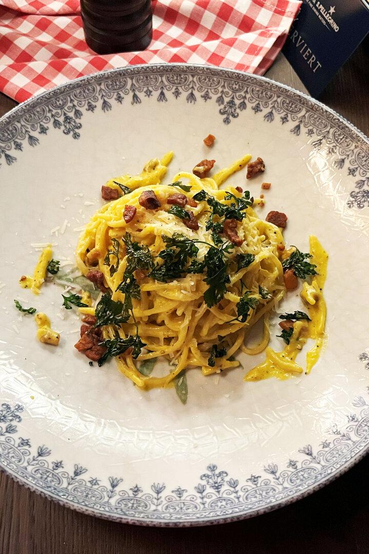 Ein Teller Spaghetti Carbonara mit Speck und Petersilie auf einem verzierten Teller.