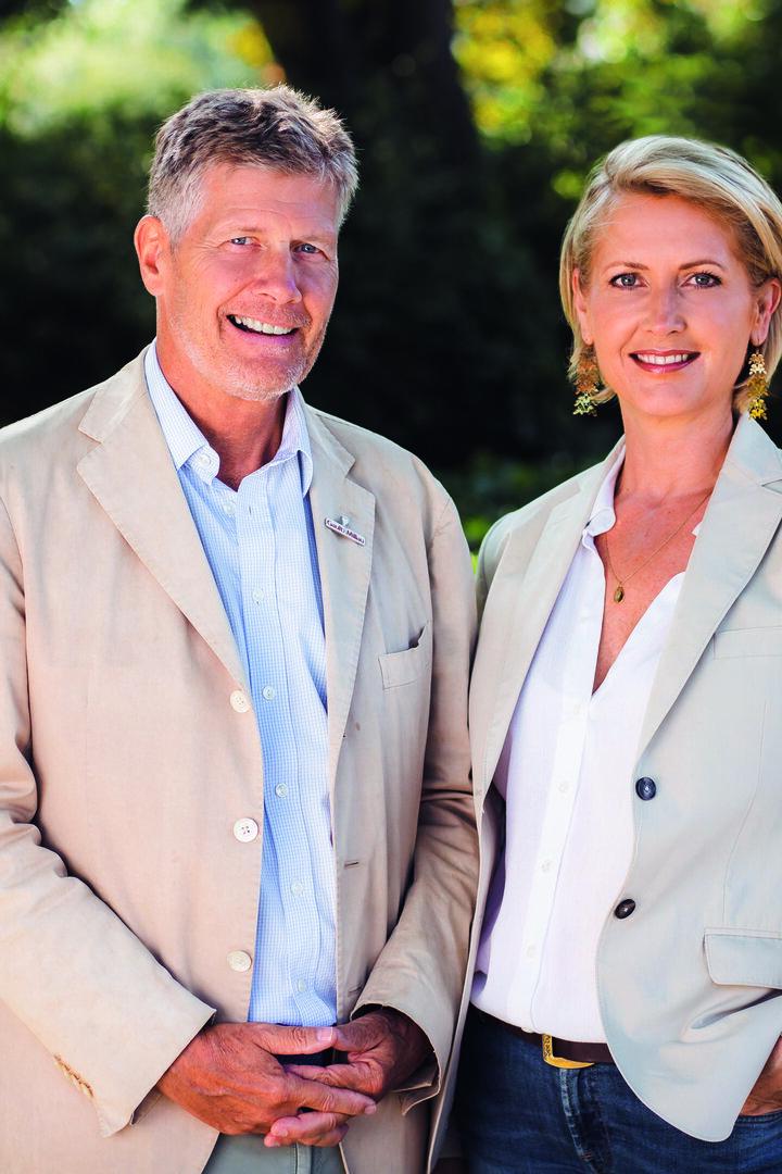 Ein Mann und eine Frau stehen lächelnd vor einem grünen Hintergrund.