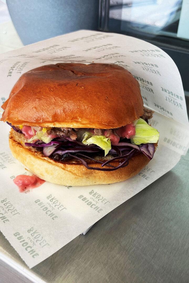 Ein Brioche-Burger mit Salat und rotem Kraut in einer Papierverpackung.
