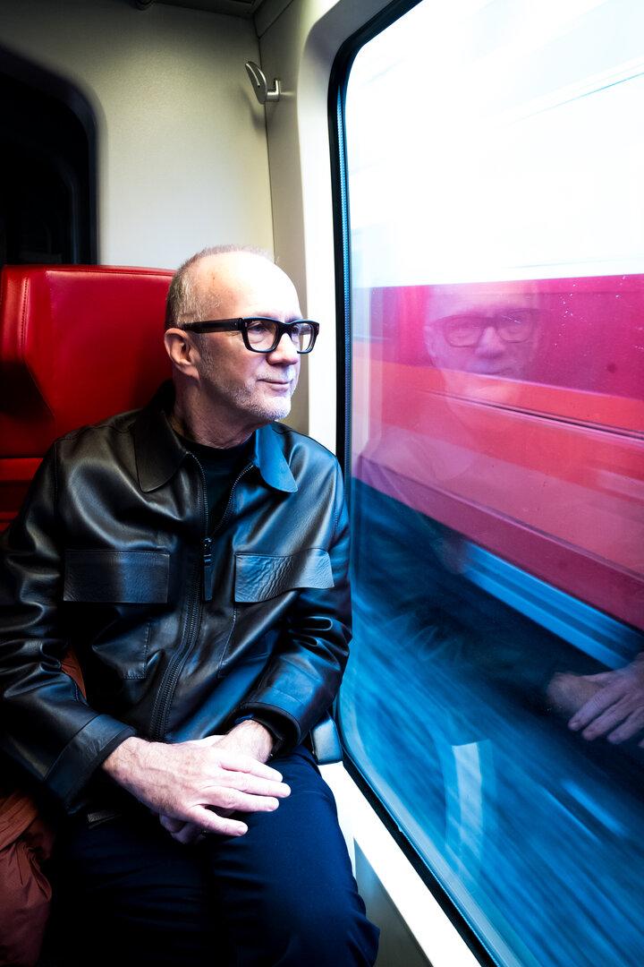 Ein Mann mit Brille sitzt in einem Zug und schaut aus dem Fenster.