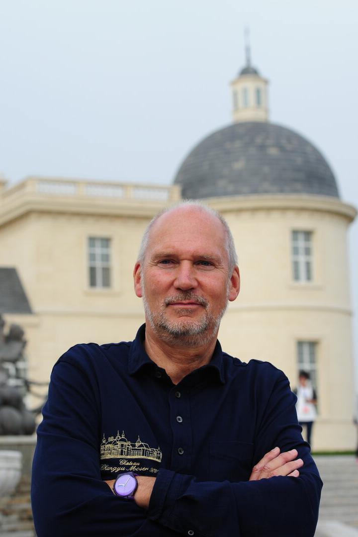 Ein Mann steht vor einem Gebäude mit Kuppeln und verschränkt die Arme.