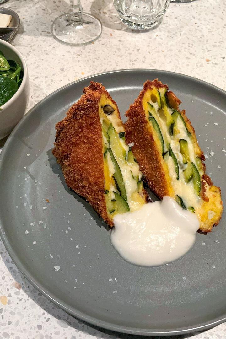 Ein Teller mit frittierten Zucchinischeiben und einer weißen Soße, dazu ein Schälchen Salat.