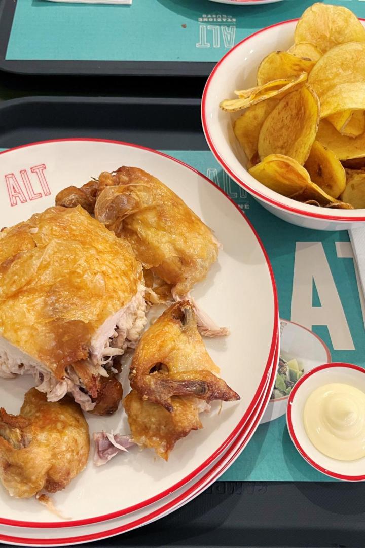 Ein Teller mit gebratenem Hähnchen und eine Schüssel mit Kartoffelchips auf einem Tablett.