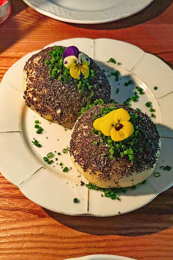 Zwei Käseknödel, garniert mit Schnittlauch und essbaren Blüten, auf einem Teller.