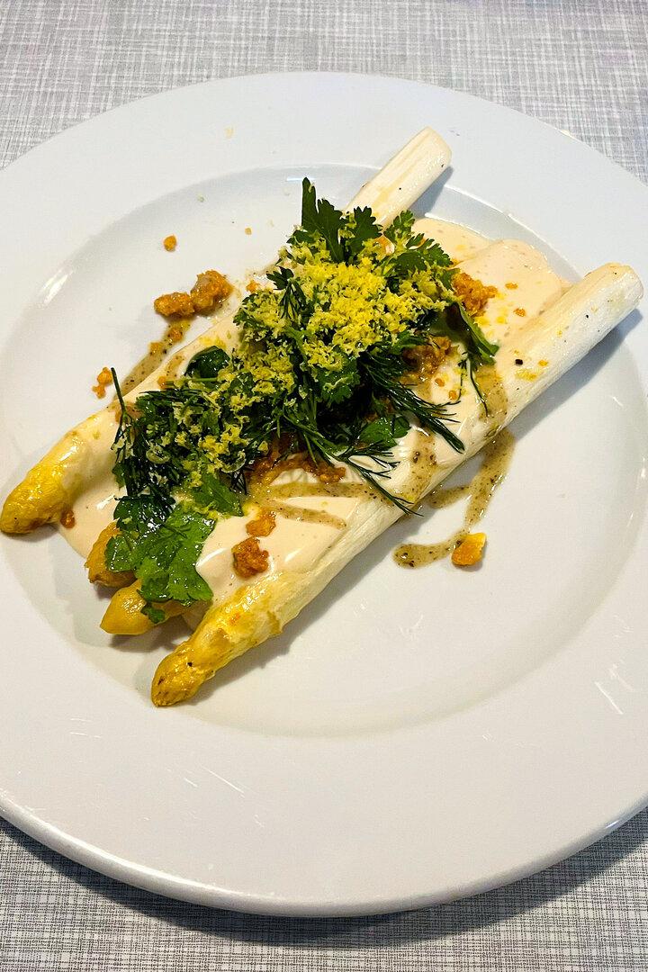 Weißer Spargel mit Sauce, Kräutern und geriebenem Ei auf einem Teller.