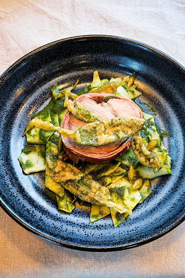Ein Teller mit Pasta, Fleisch und Pesto steht auf einem Tisch neben Messer und Gabel.