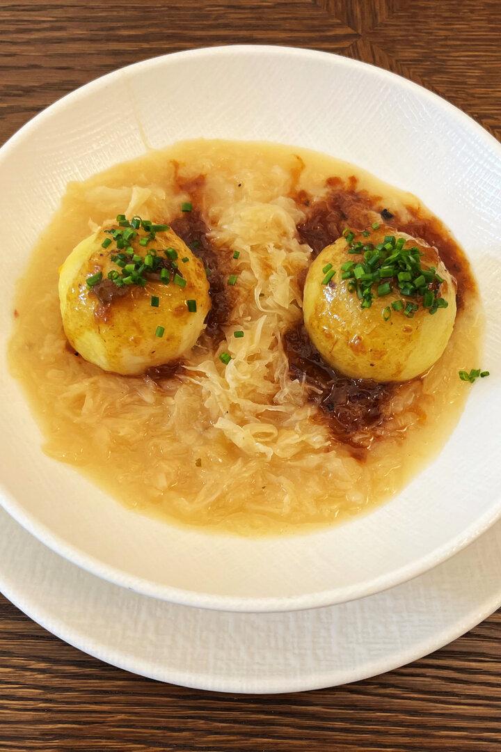 Zwei Kartoffelknödel mit Soße und Sauerkraut auf einem Teller.