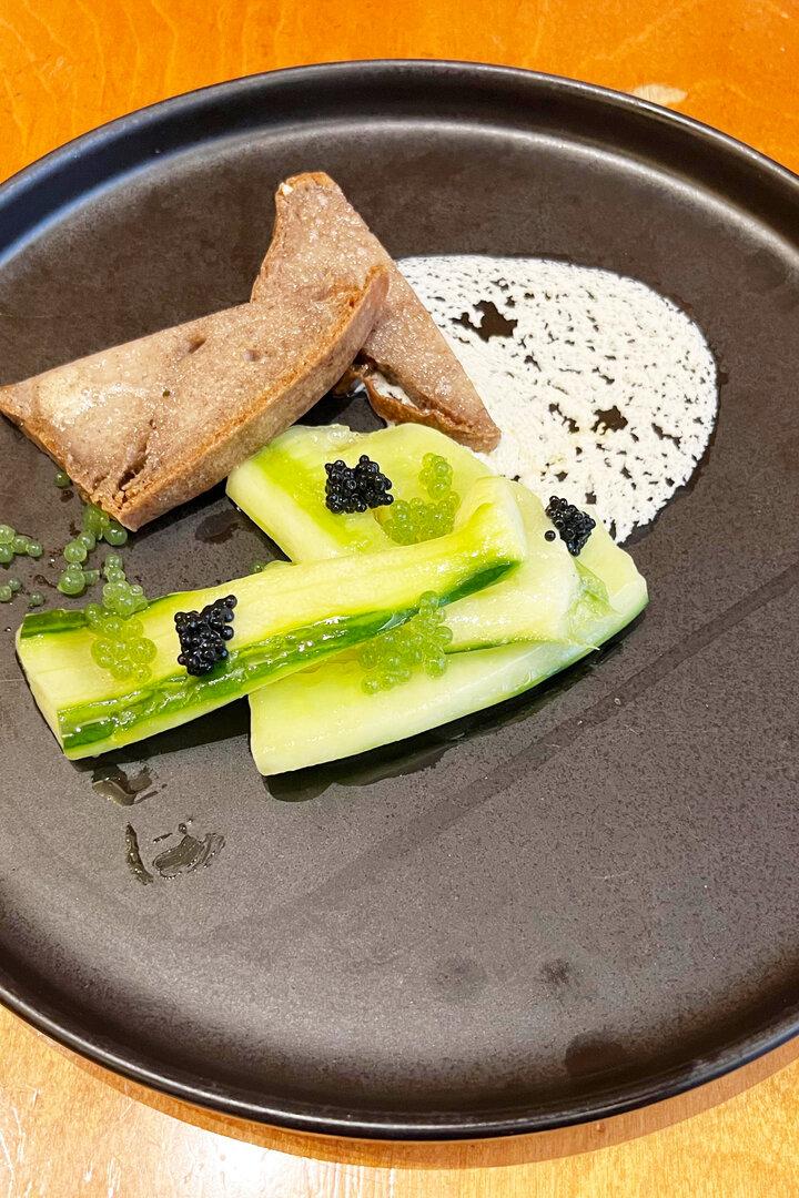Ein Teller mit Gurkenscheiben, Brot, Kaviar und einer weißen Soße.