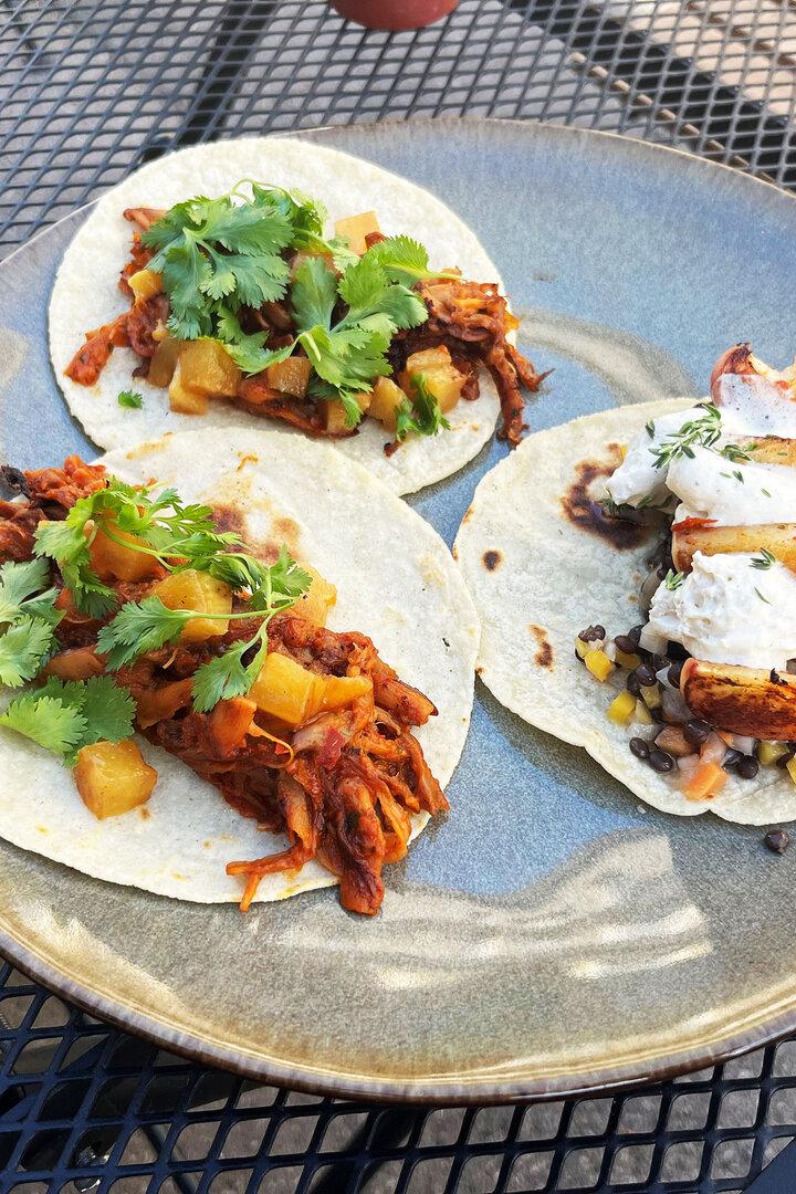 Drei Tacos auf einem Teller, einer mit Pfirsich und zwei mit Ananas und Koriander.