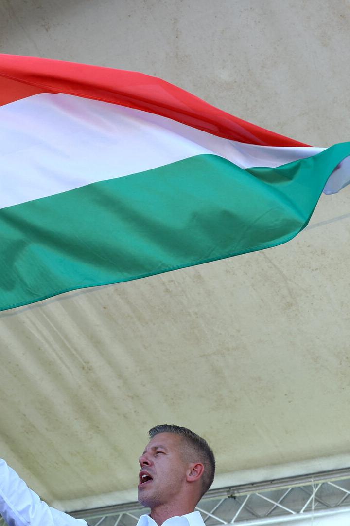 Peter Magyar steht auf einer Bühne und hält die ungarische Flagge hoch