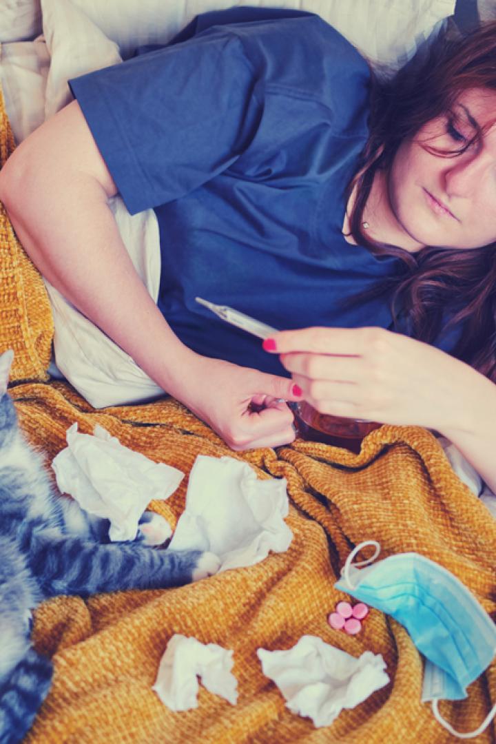 Frau mit Fieberthermometer und Katze im Bett