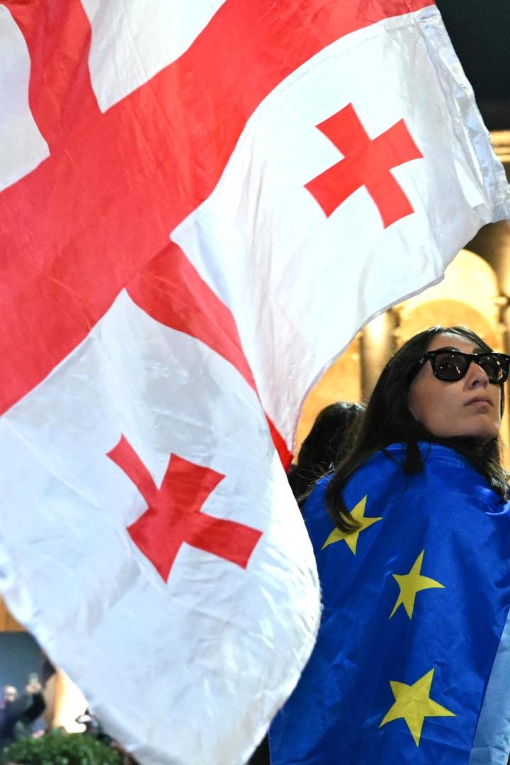 Eine Frau schwenkt eine Georgien-Flagge, sie hat eine EU-Flagge umgehängt.