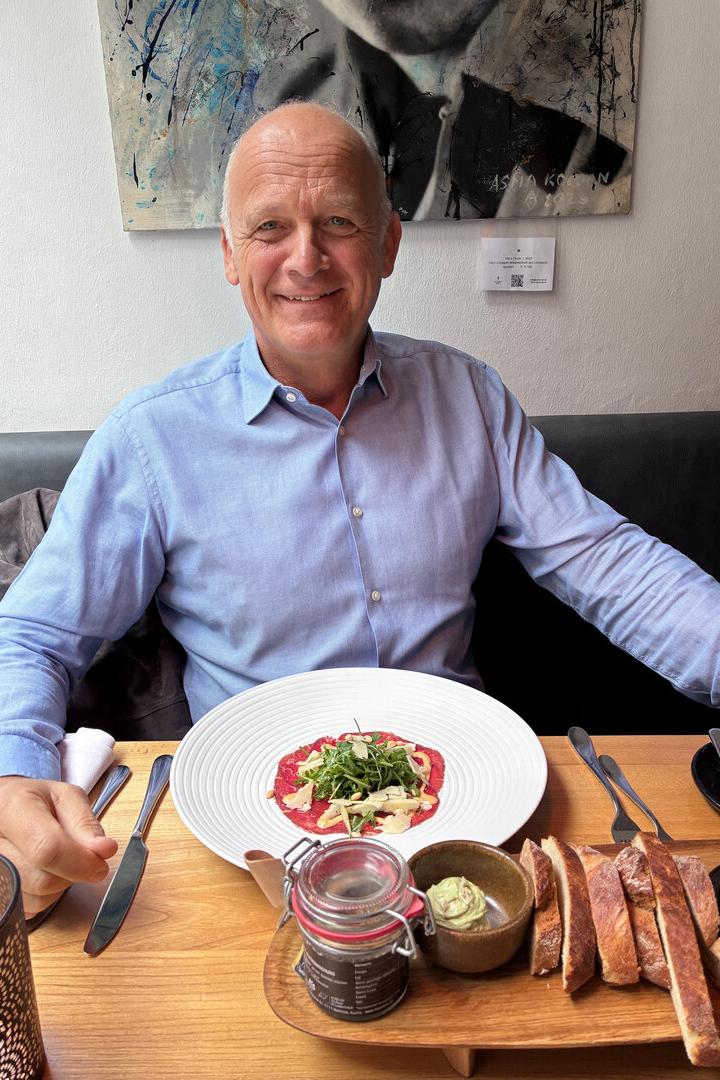 Herwig Straka, Sportmanager Herwig Straka sitzt in blauem Hemd am Restauranttisch, vor sich ein Rindscarpaccio