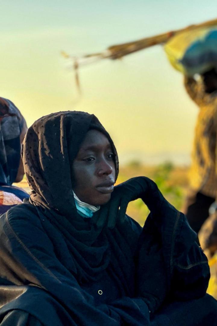 Eine Frau sitzt am Boden, dahinter gehen Menschen vorbei.