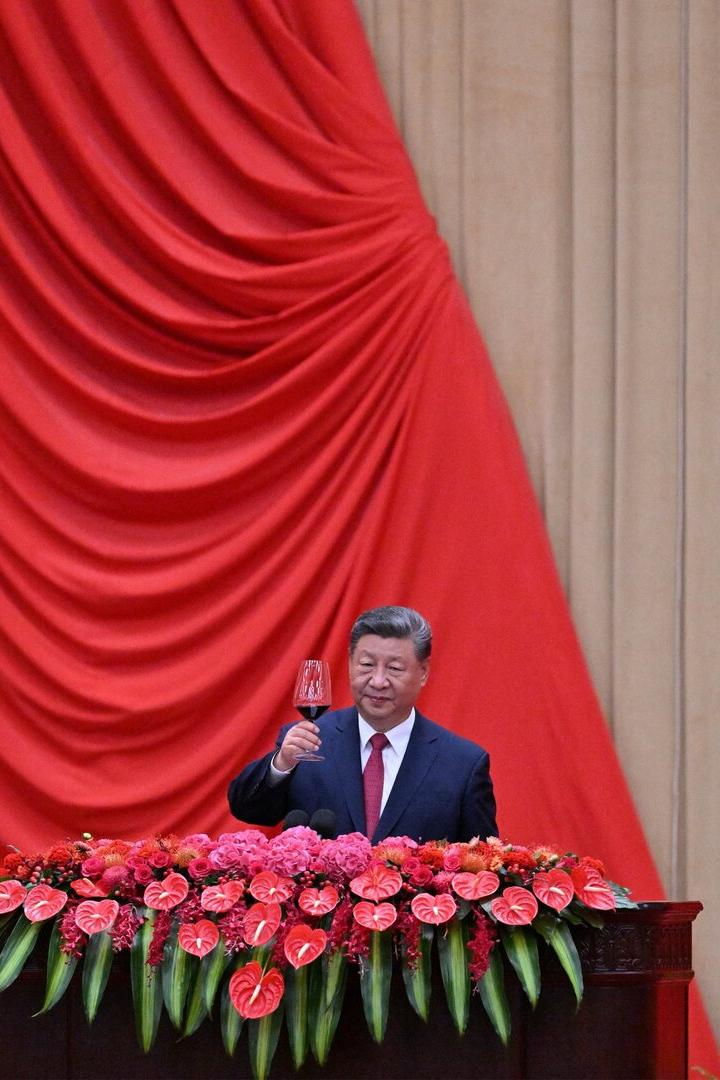 Chinas Präsident Xi Jinping prostet mit einem Glas Rotwein von einem blumengeschmückten Pult