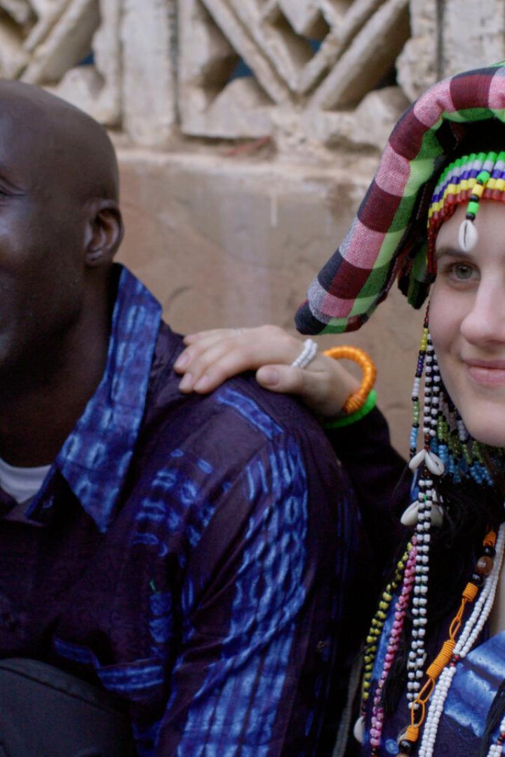 Victoria Preuer und Siaka Touray sind ein Paar. Sie, mit traditionellem Kopfschmuck, legt ihre Hand auf die Schulter des lächelnden Mannes.