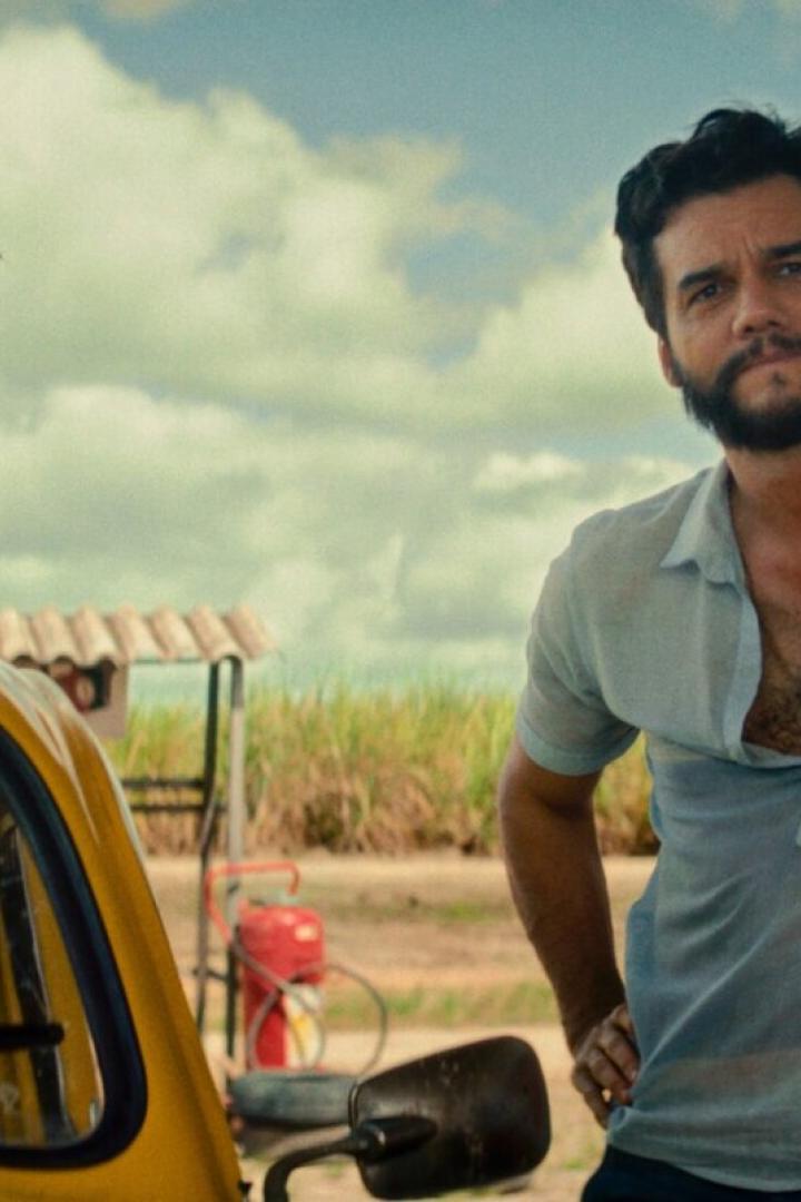 Der Schauspieler Wagner Moura lehnt an einer Säule, neben ihm ein gelbes Auto