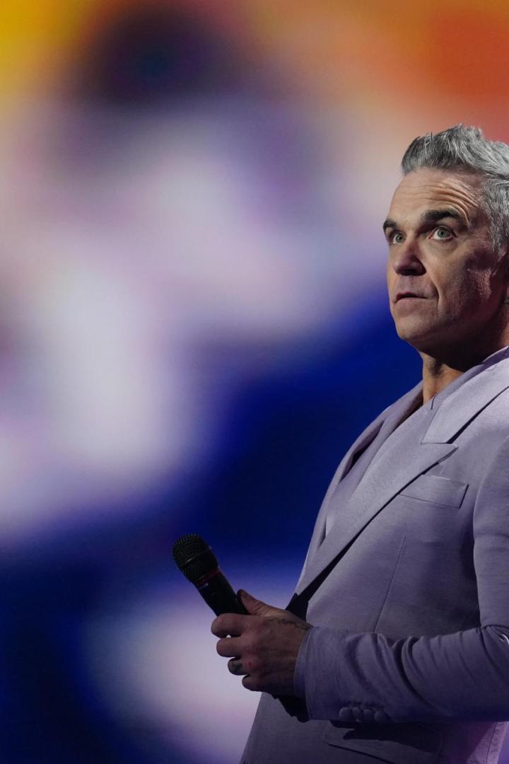 Robbie Williams im blasslila Anzug mit Mikro auf der Bühne