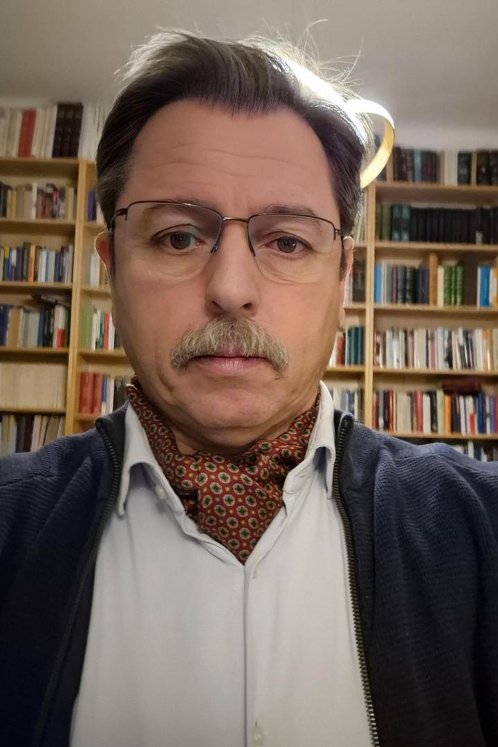 Walter Posch steht vor einem Bücherregal.