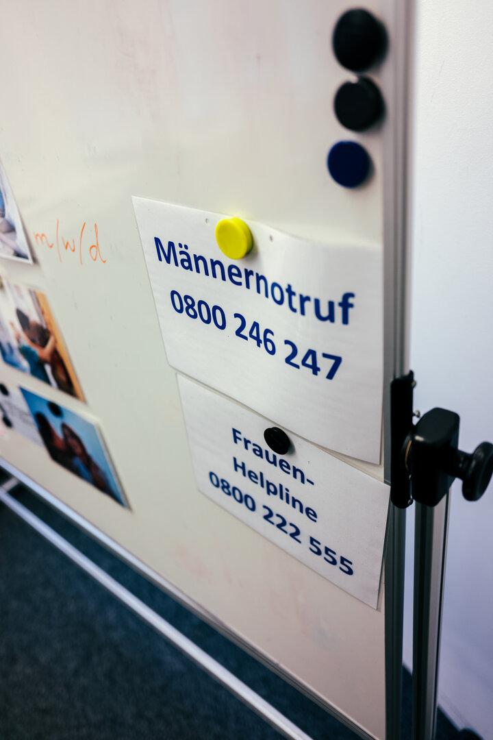 Telefonnummern des Männernotrufs und der Frauenhelpline auf einem Whiteboard