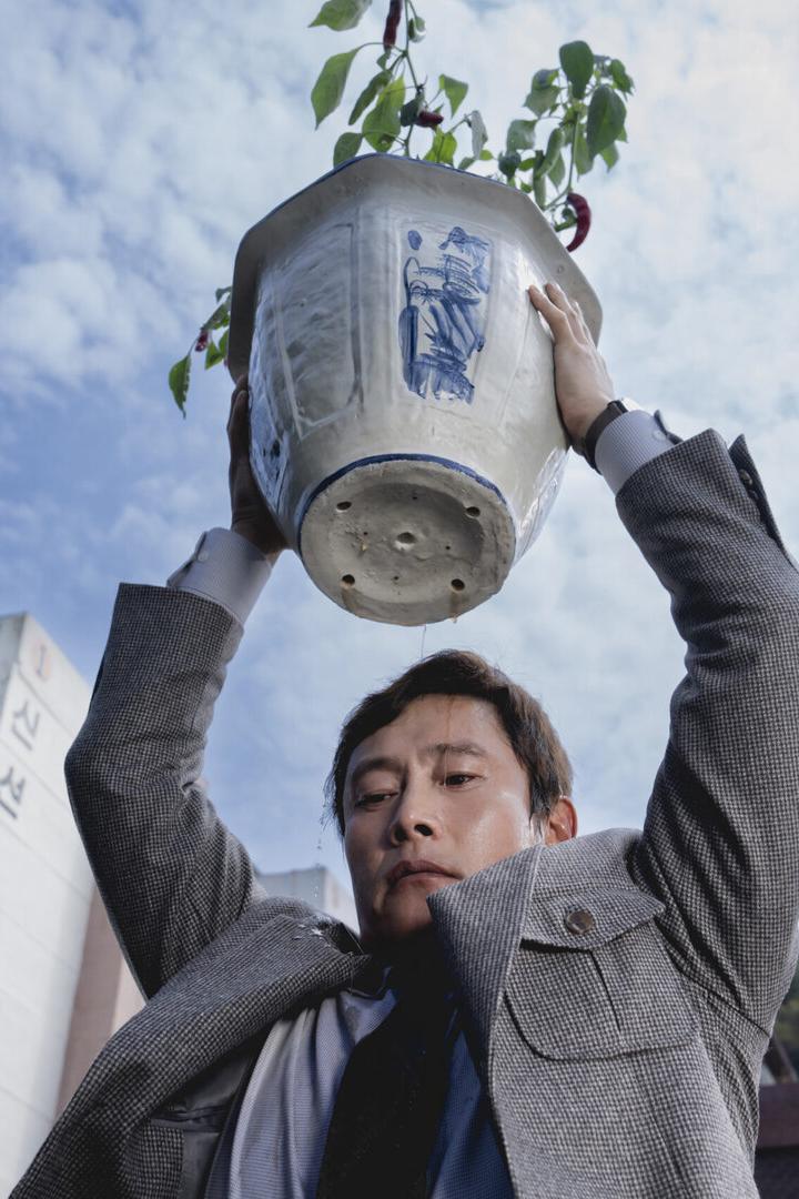 Der Schauspieler Lee Byung-hun, von unten gesehen, mit einem großen Blumentopf, den er wie wurfbereit über seinen Kopf hält 