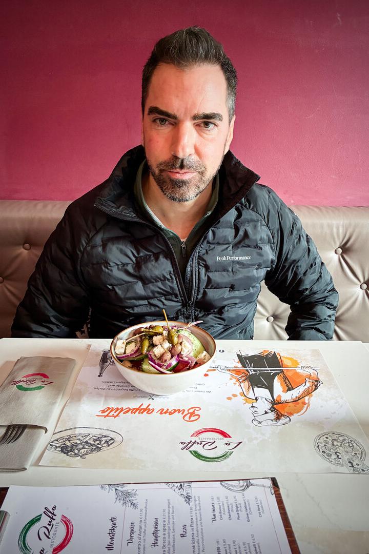 Unternehmer Karl Ochsner sitzt in einer Daunenjacke in einer Pizzeria, vor sich am Tisch ein Salat