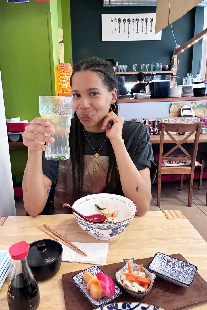 Rebecca Horner sitzt an einem Tisch, vor sich asiatische Speisen, in der Hand ein großes Glas Soda-Zitron