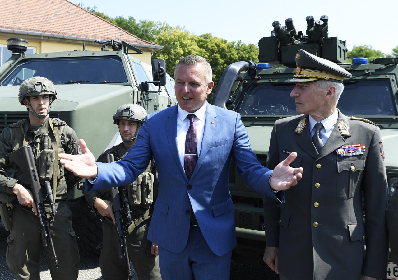Mario Kunasek und ein Offizier stehen vor Militärfahrzeugen, flankiert von Soldaten.