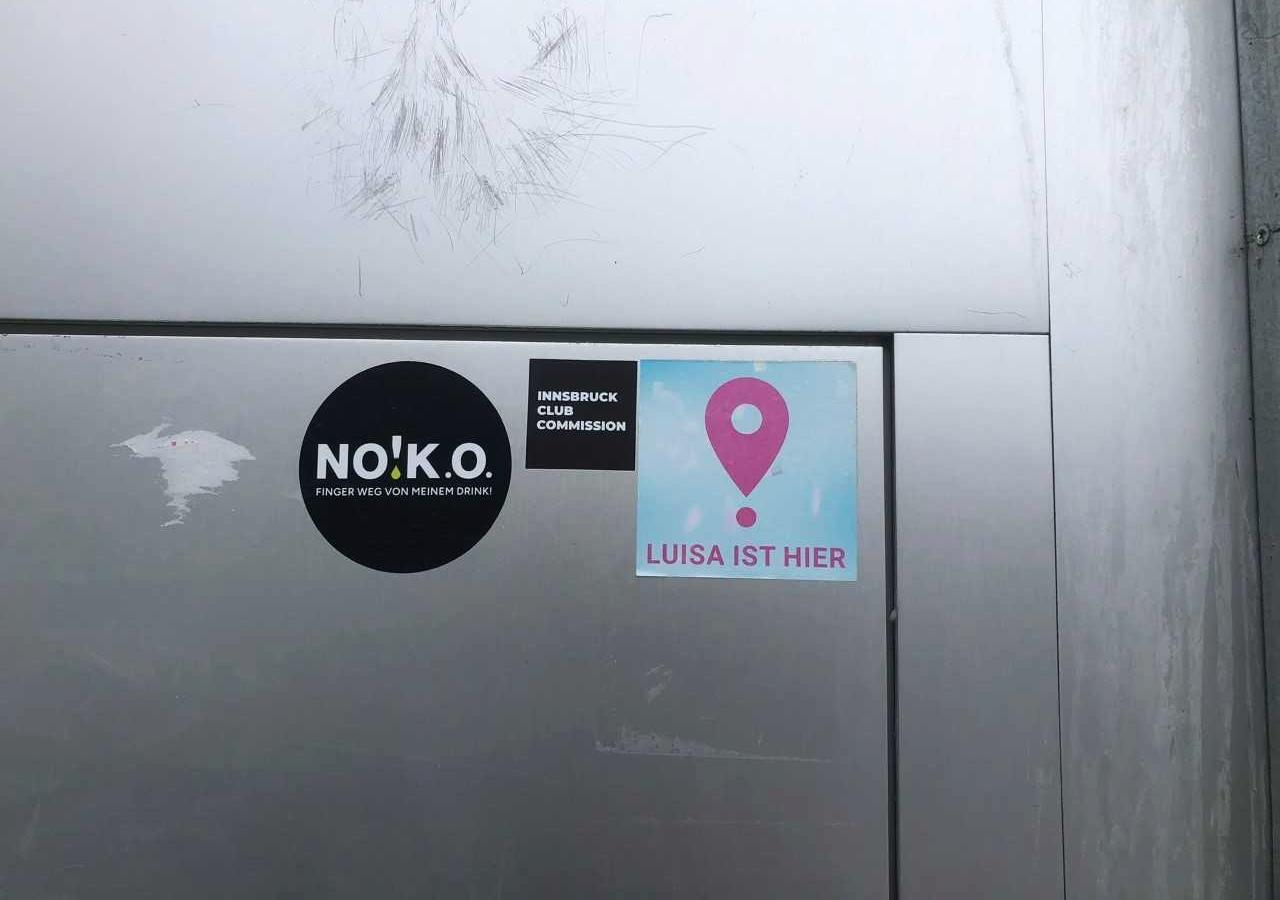 Man sieht die Tür eines Clubs in Tirol, auf der die Sticker der "Luisa-ist-hier"- Kampagne und der Sticker der Innsbruck Club Commission kleben