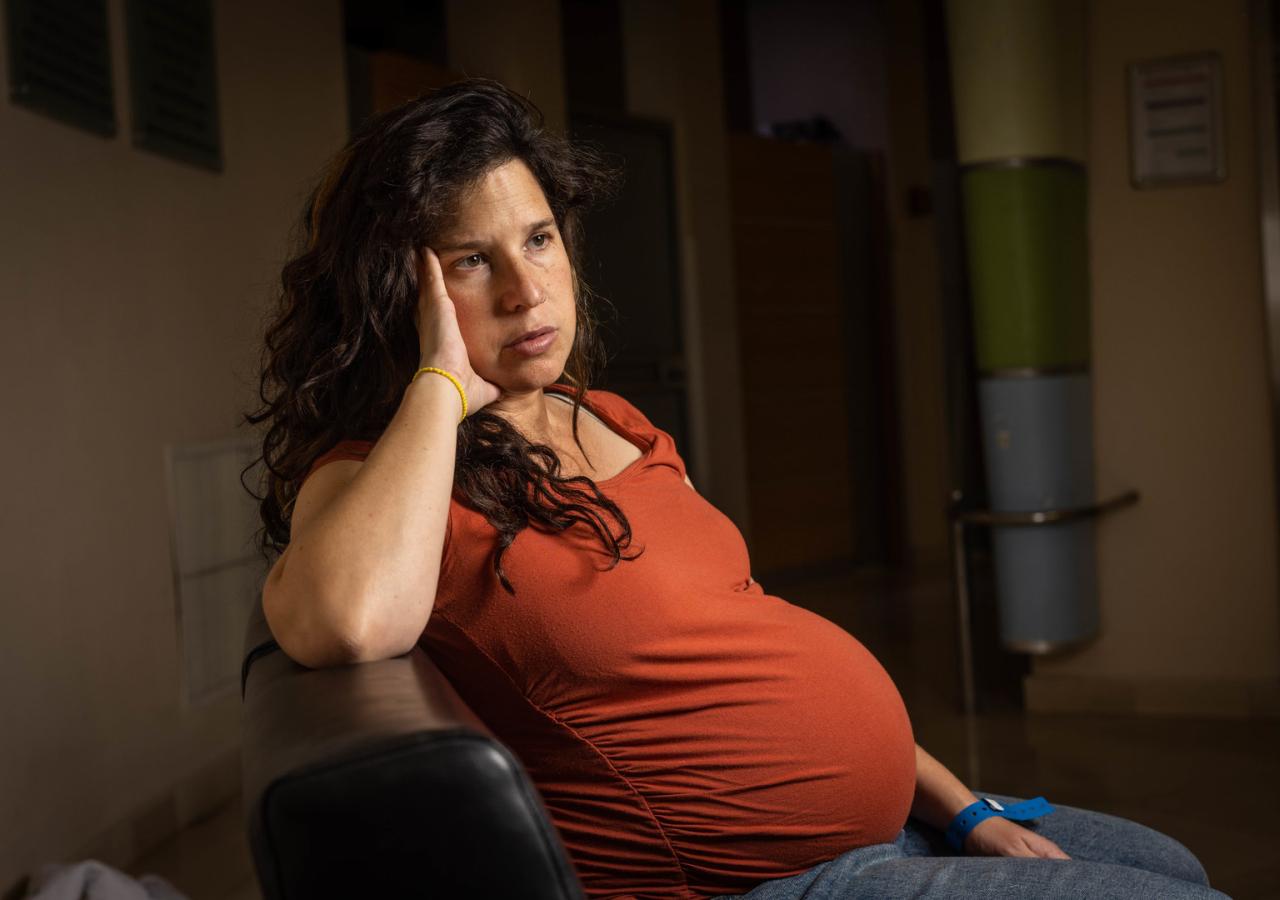 Eine schwangere Frau sitzt mit nachdenklichem Blick in einem Sessel.