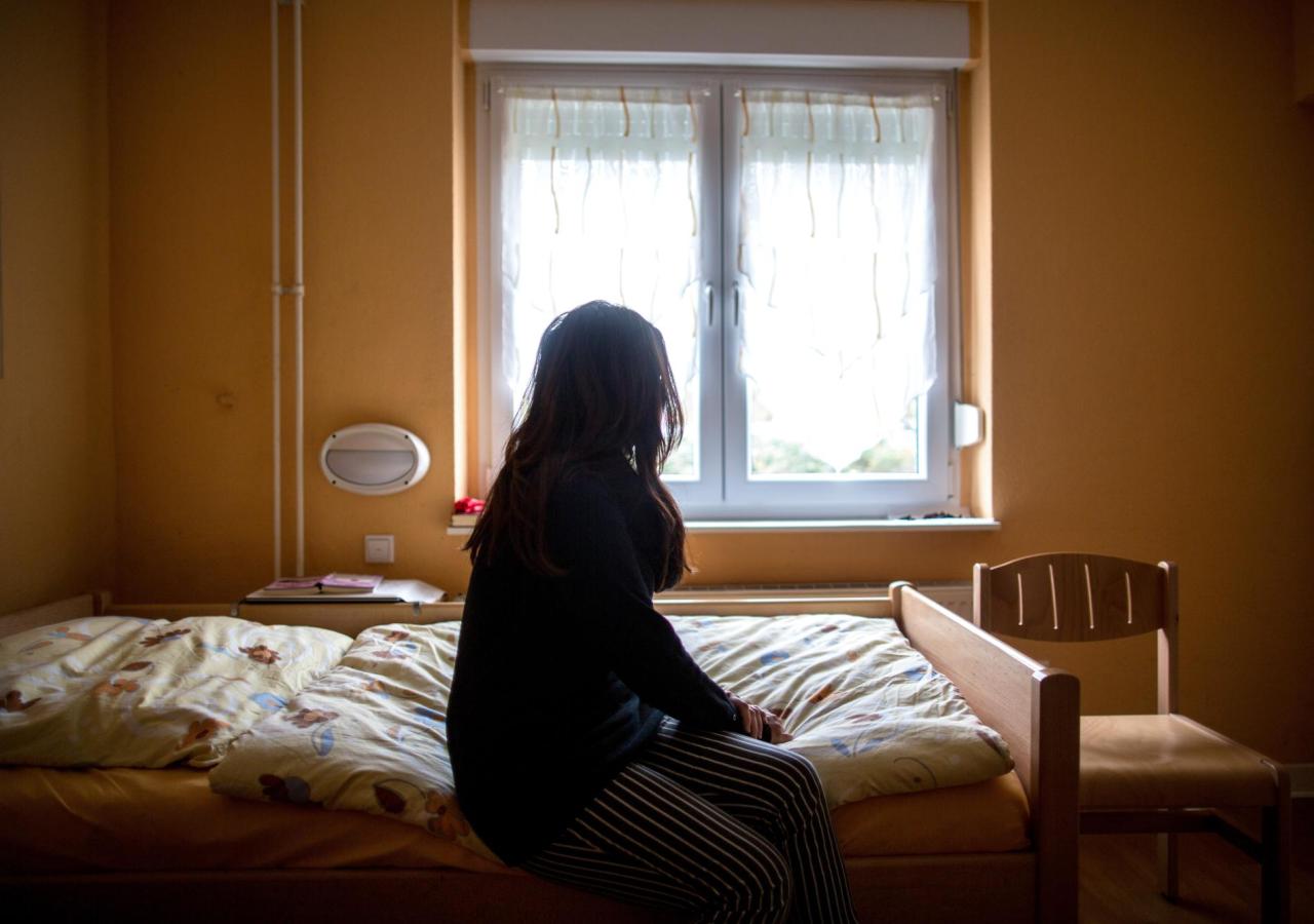 Eine Frau sitzt in einem Frauenhaus auf einem Bett. Frauenhäuser bieten Schutz, wenn der Partner zur Gefahr wird. Dieses Foto stammt von einer Agentur.