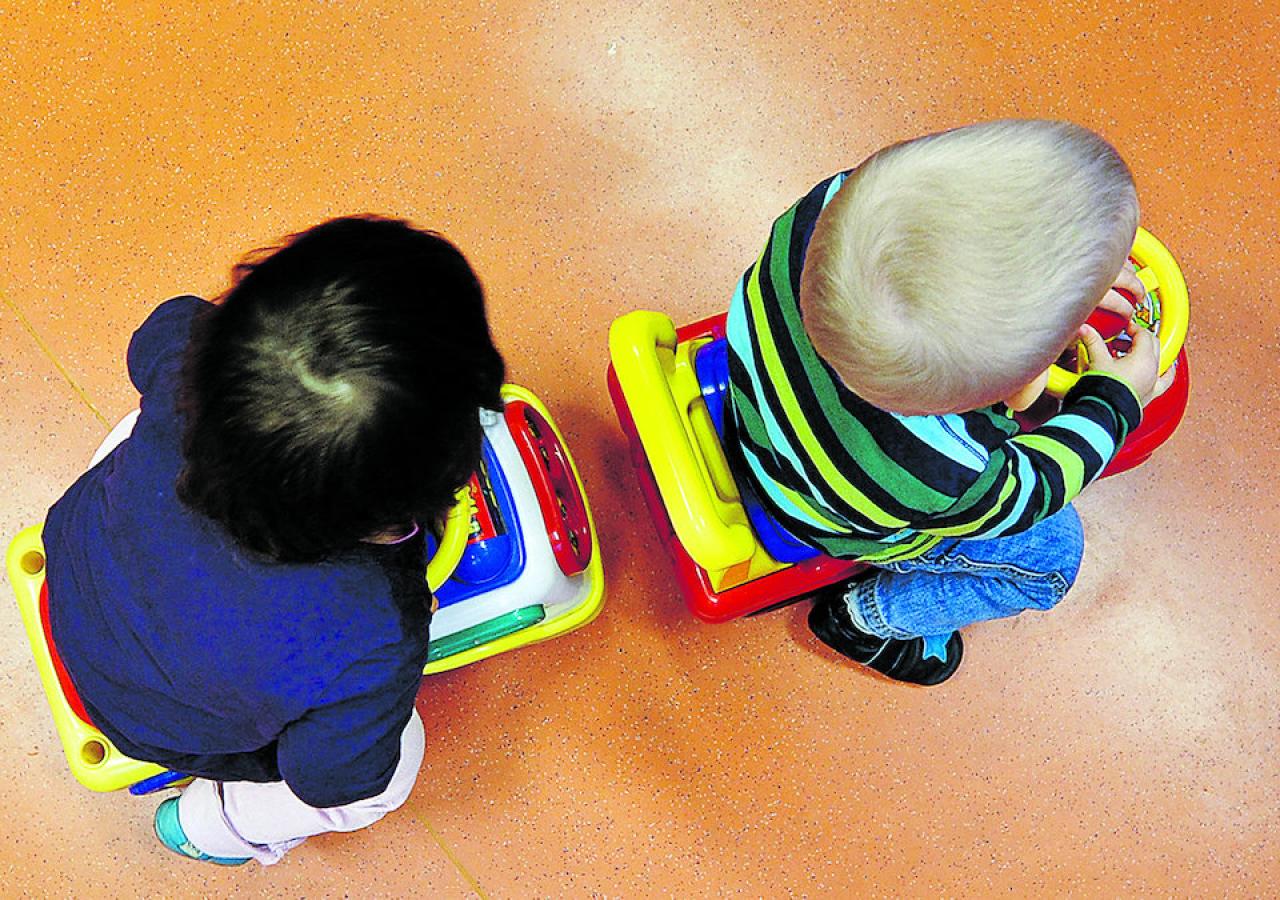 Zwei kleine Kinder spielen mit bunten Spielzeugautos auf einem orangefarbenen Boden.