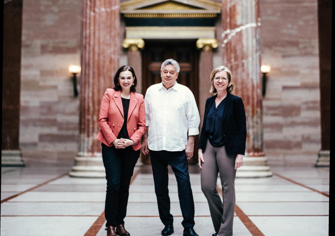Alma Zadić, Werner Kogler und Leonore Gewessler posieren vor einem Gebäude mit Säulen.