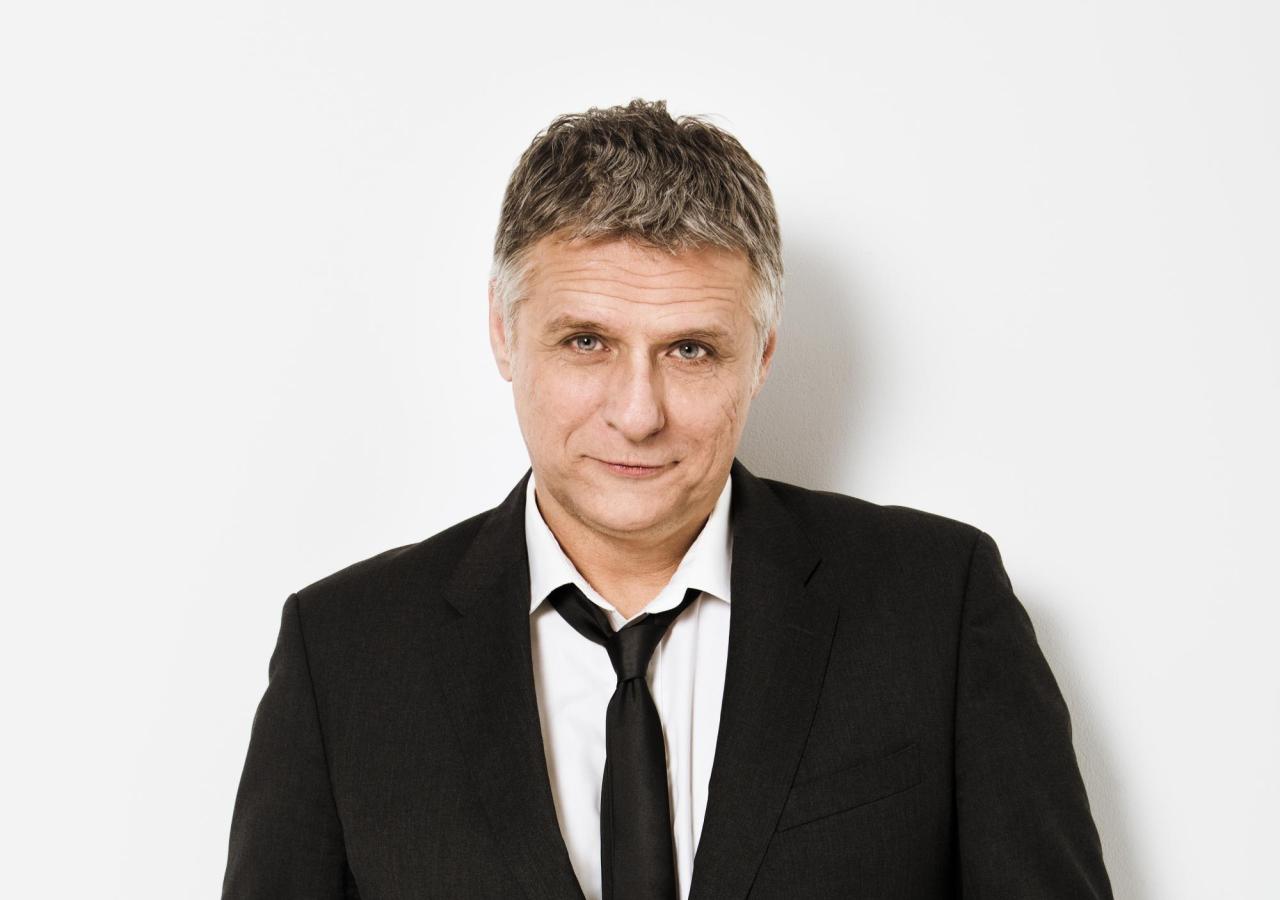 Rainer Nikowitz in einem dunklen Anzug mit Krawatte.