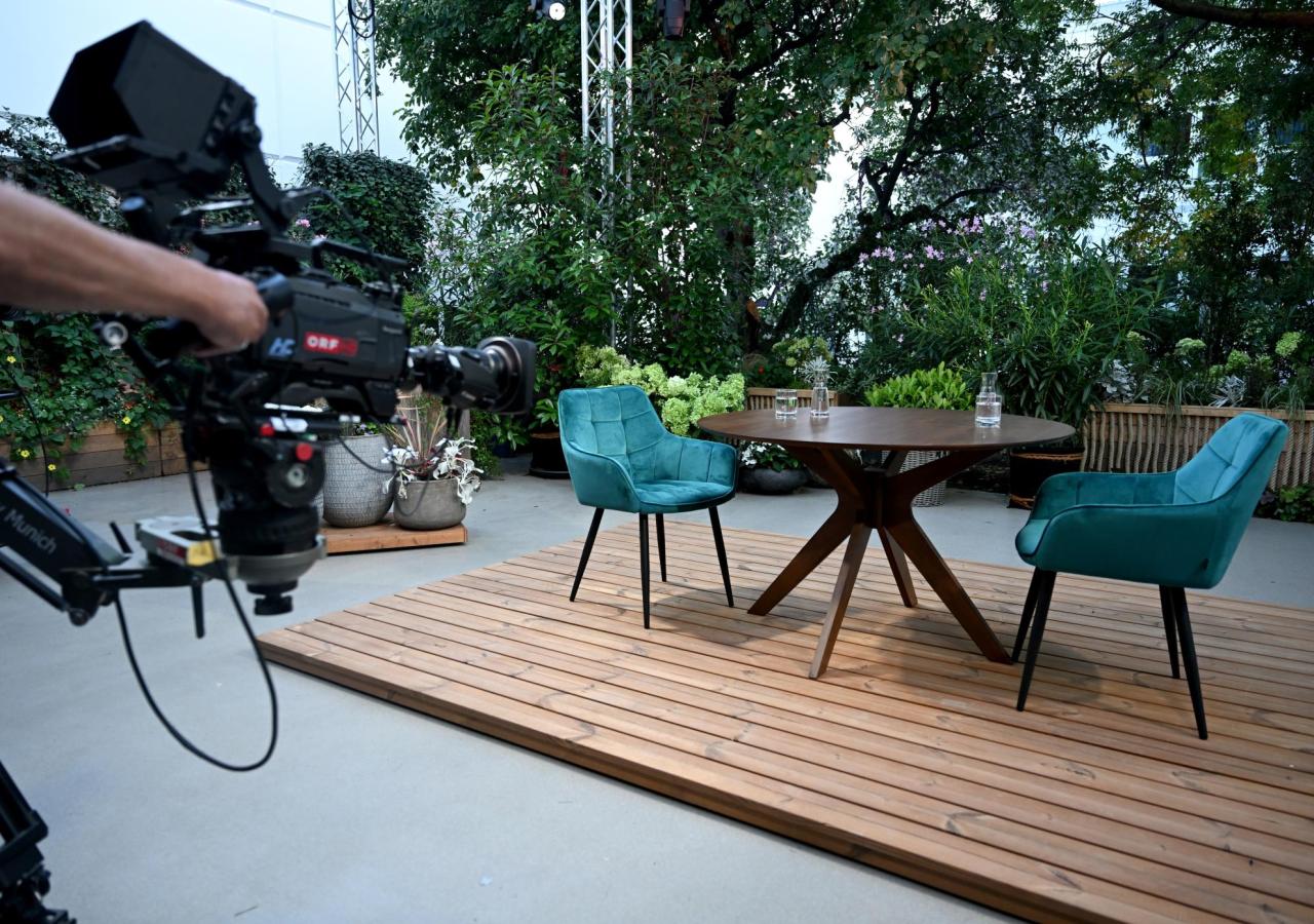zu sehen ist das Setting der ORF-Sommergespräche 2025: ein großer brauner Tisch und zwei blaue Stühle