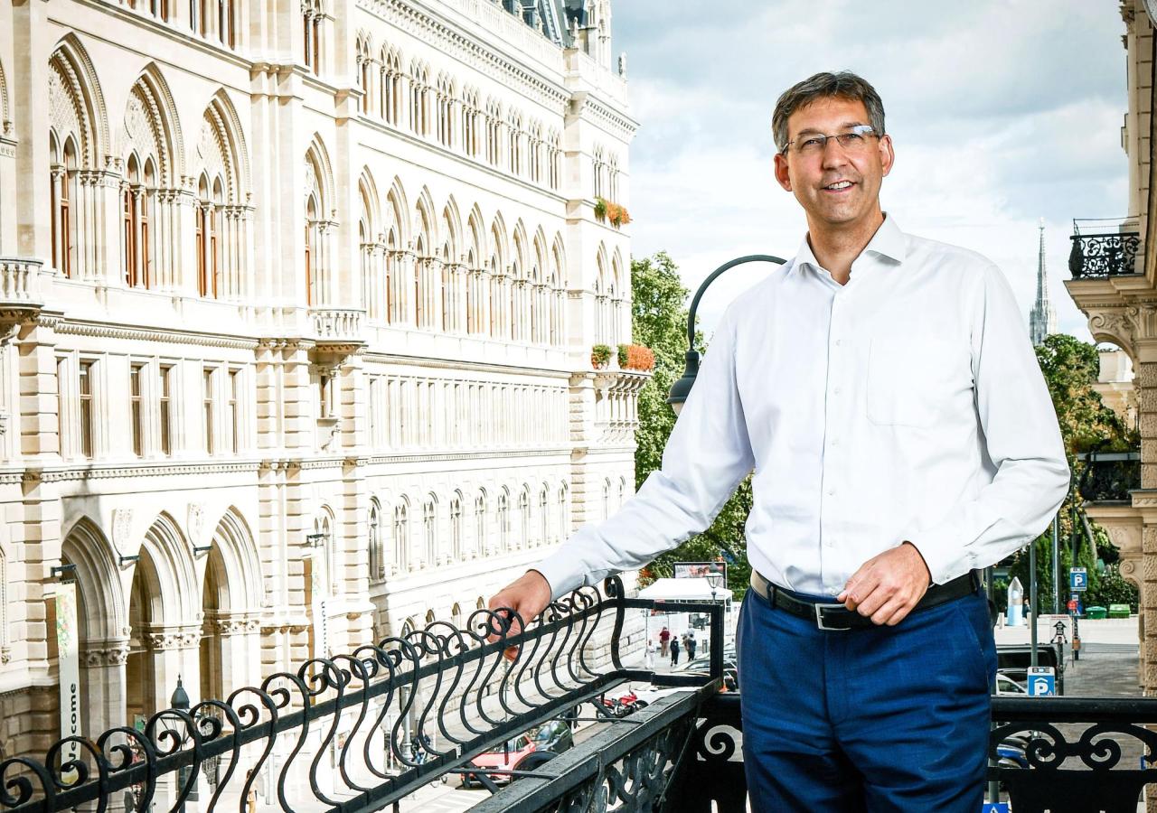 Ein Mann im weißen Hemd steht lächelnd auf einem Balkon. Es handelt sich um den Chef der Wiener ÖVP, Markus Figl. Daneben ist die Fassade des Wiener Rathauses zu sehen.