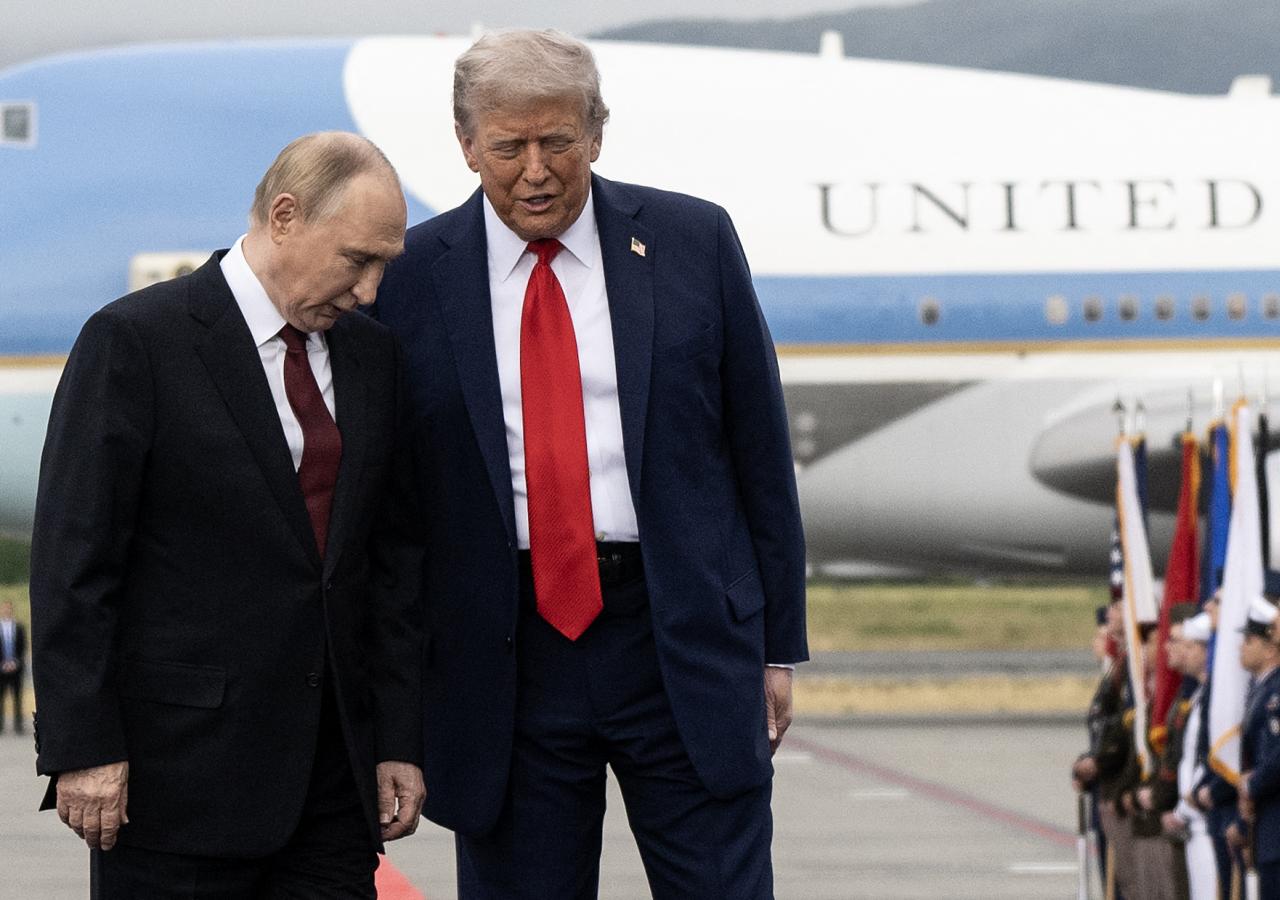 Russlands Präsident Putin und US-Präsident Trump stehen nebeneinander auf einem Flughafen-Rollfeld vor einem Flugzeug, im Hintergrund stehen Soldaten