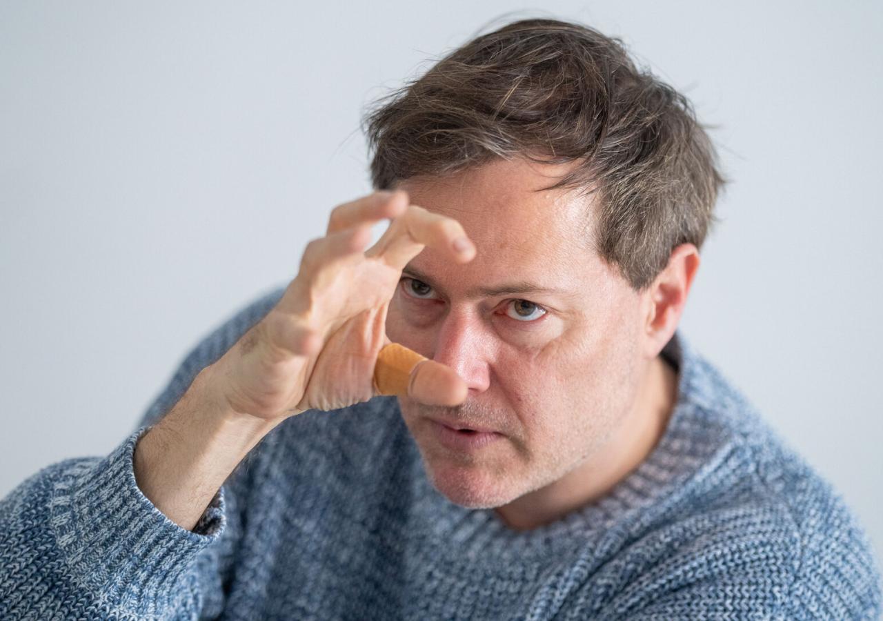 Festwochen-Intendant Milo Rau Mann in blauem Pullover hält seine rechte Hand mit ausgestreckten Fingern, als wollte er etwas packen, vors Gesicht