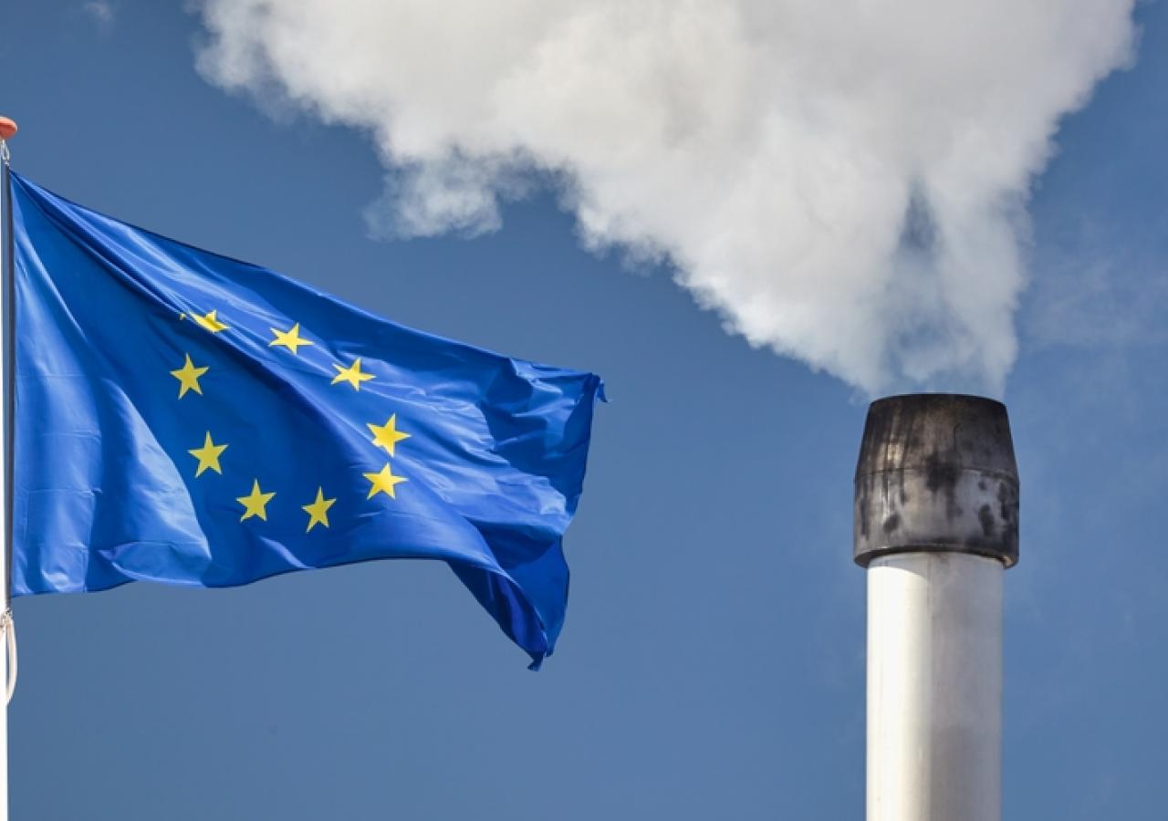 Bremsen beim Klimaschutz Eine EU-Fahne weht vor einem Fabriksschlot, der Rauch ausstößt