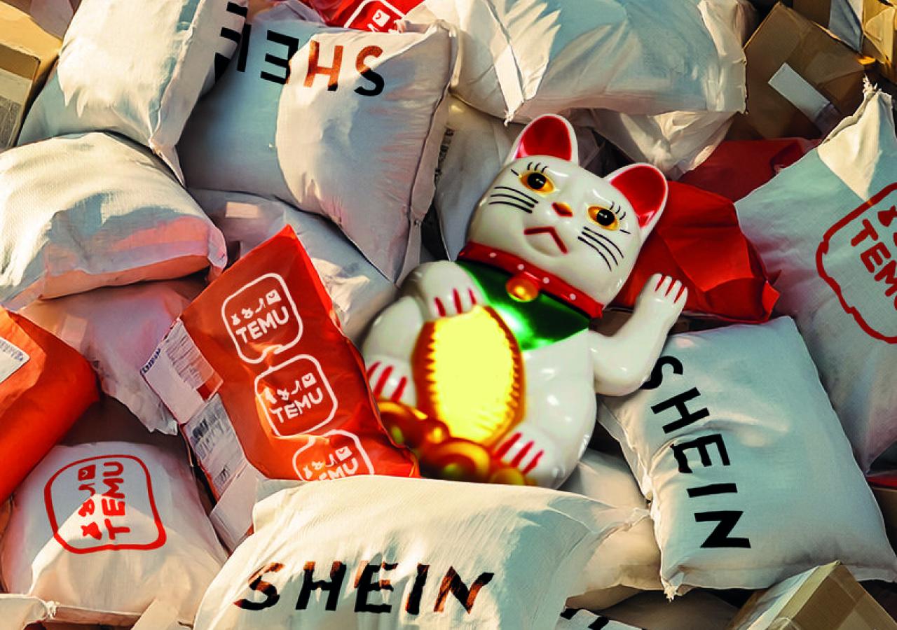 Ein Haufen Plastikbeutel von Shein und Temu, dazwischen liegt eine chinesische Winkekatze.
