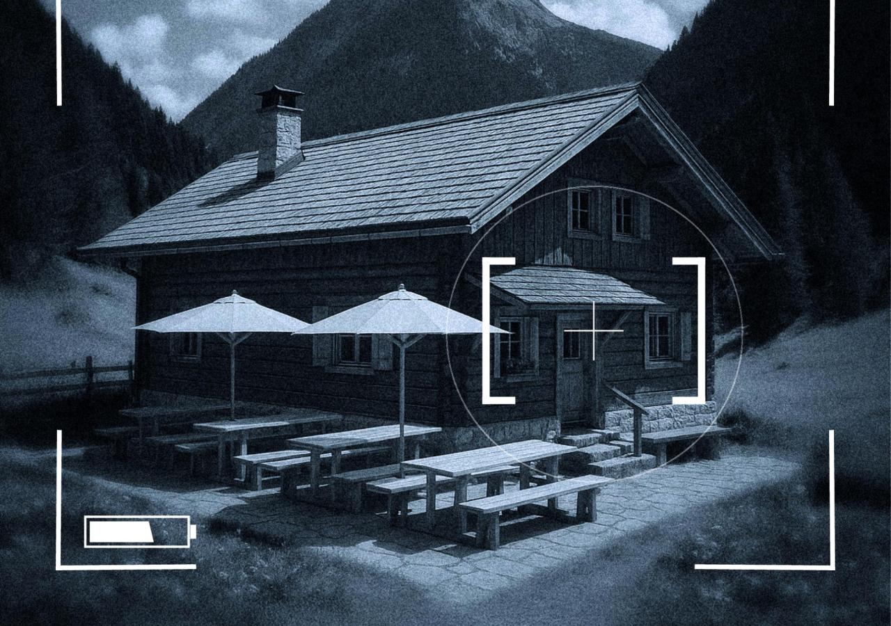 Berghütte mit Holzbänken und Sonnenschirmen, umgeben von Bergen, im Fadenkreuz dargestellt. Die Finanzpolizei jagt auch dort nach Steuerfahndern.