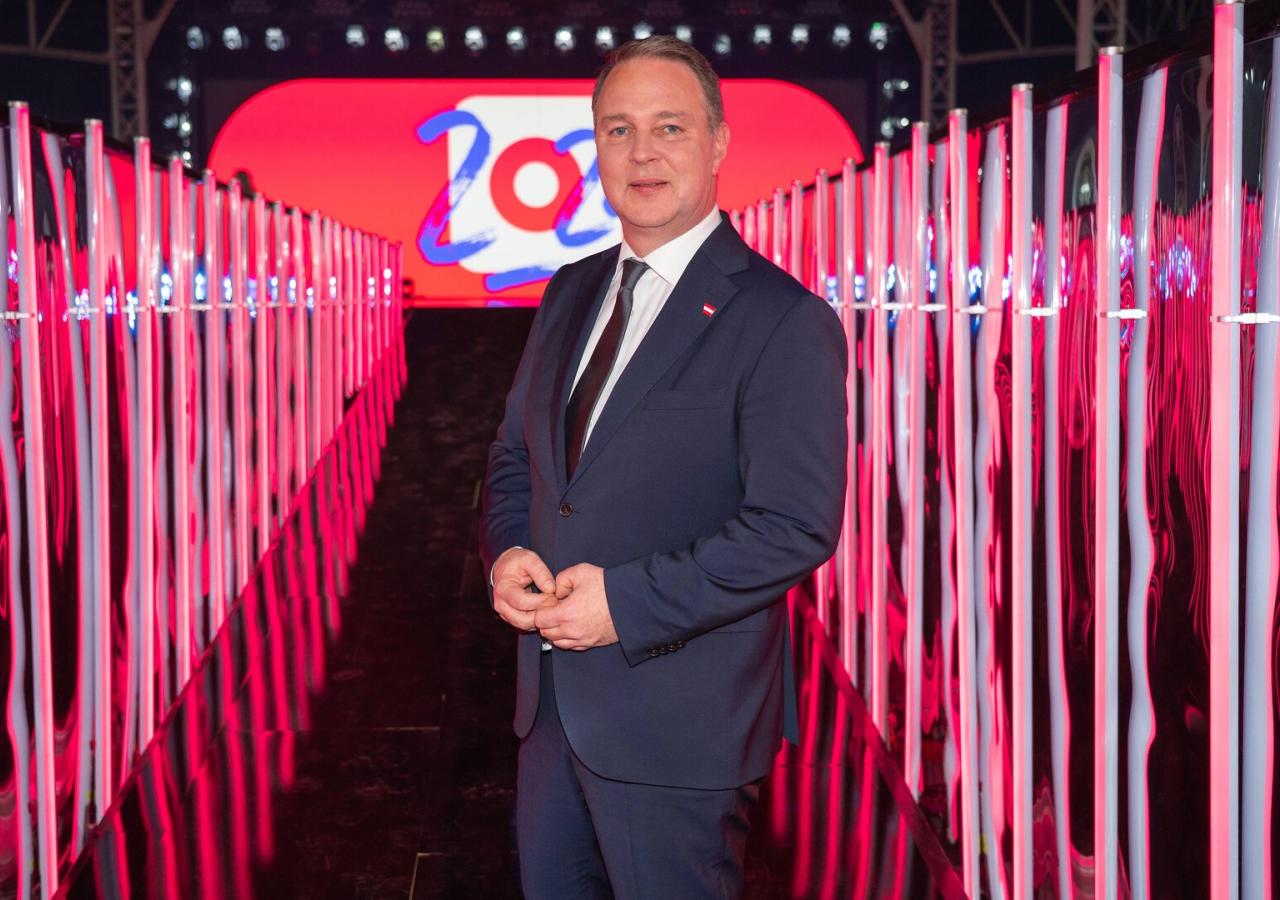 Mann in dunkelblauem Anzug posiert in einem rosaroten, neonbeleuchteten Korridor.