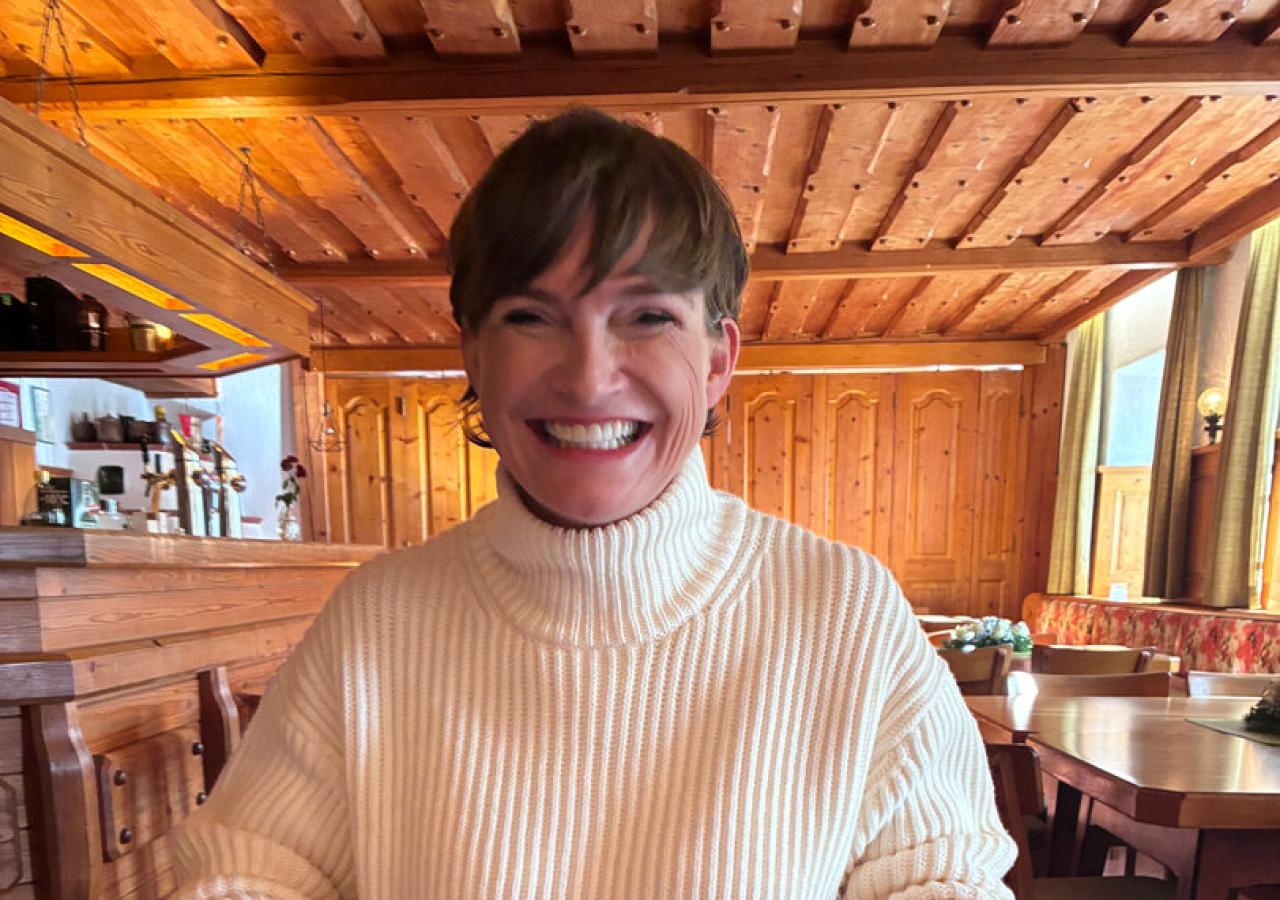 Astrid Steharnig-Staudinger sitzt in einem leeren Wirtshaus mit Holzvertäfelung und isst einen Schweinsbraten