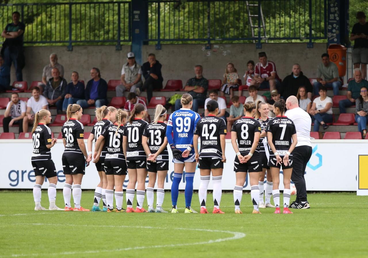 Spielerinnen des LASK stehen auf einem Fußballplatz und sind von hinten zu sehen