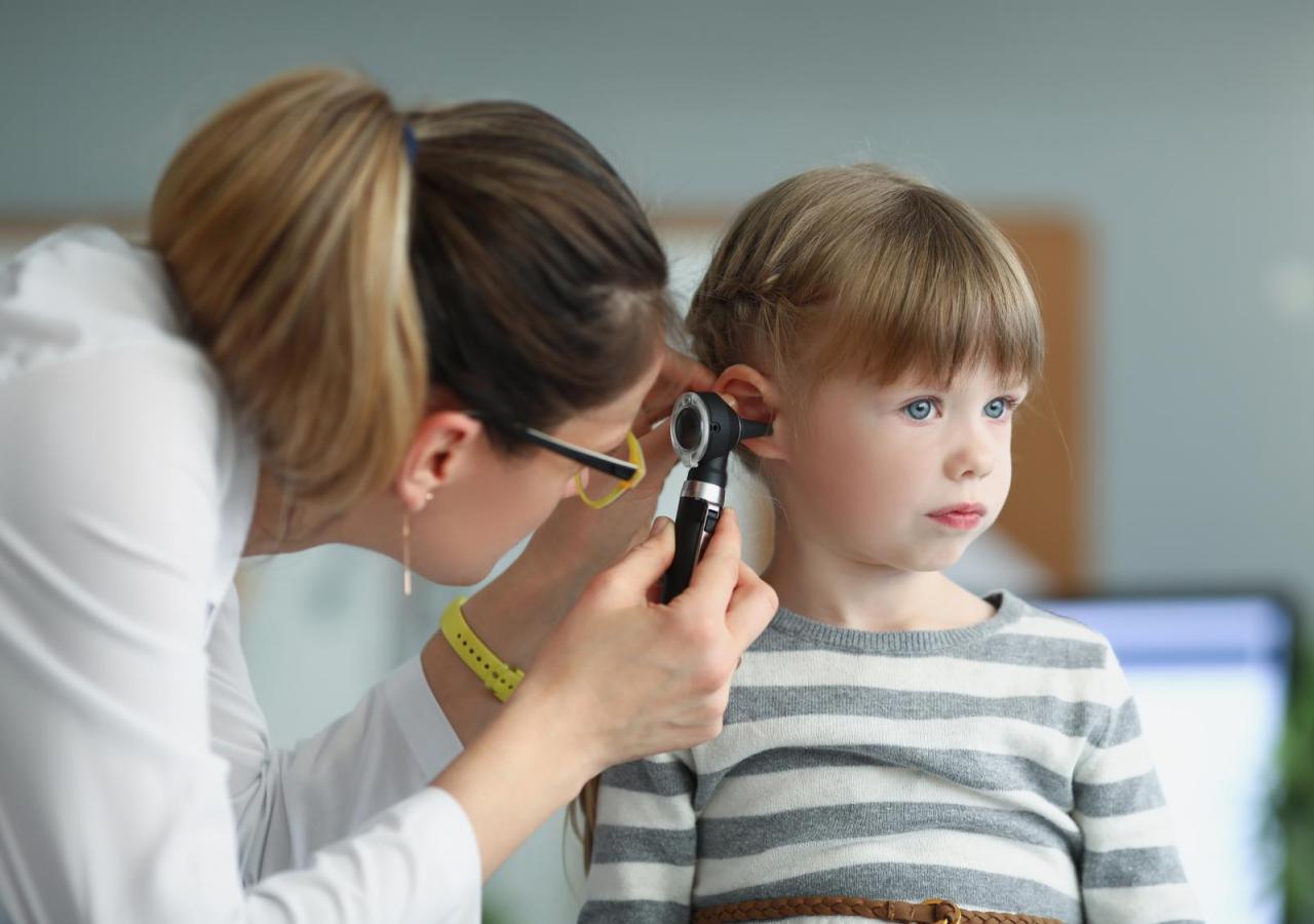 Kinderarzt mit Blick auf das Ohr eines kleinen Mädchens mit Otoskop.