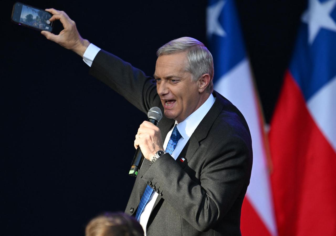 Ein Mann in Anzug (Jose Kast) spricht in ein Mikro und hält ein Handy hoch.