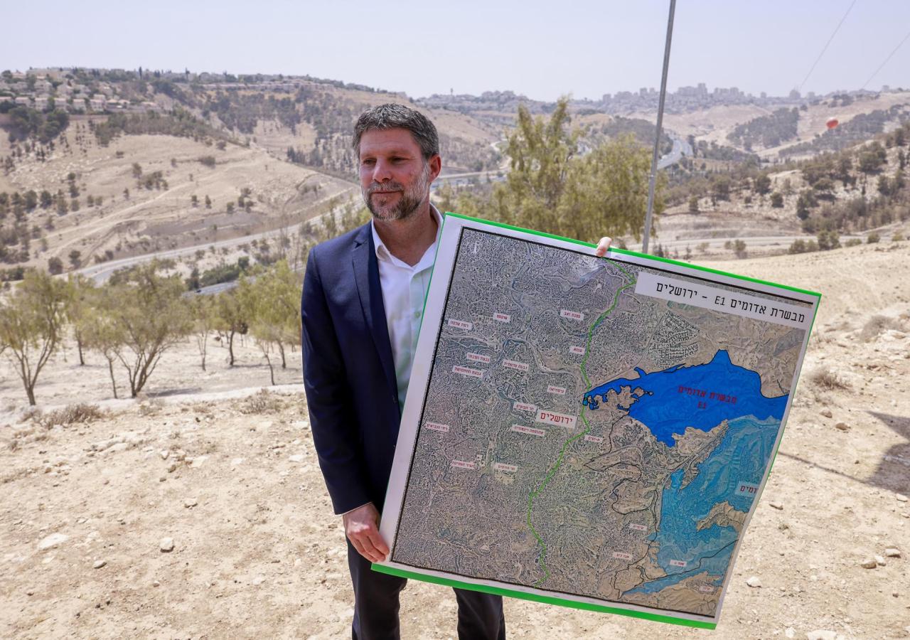 Bezalel Smotrich hält eine Karte mit einer groß blau eingezeichneten Zone hoch, dahinter Hügellandschaft.