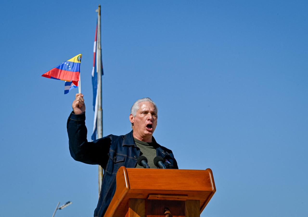 Miguel Díaz Canel schwenkt eine venezolanische Flagge, er steht vor einem Rednerpult.