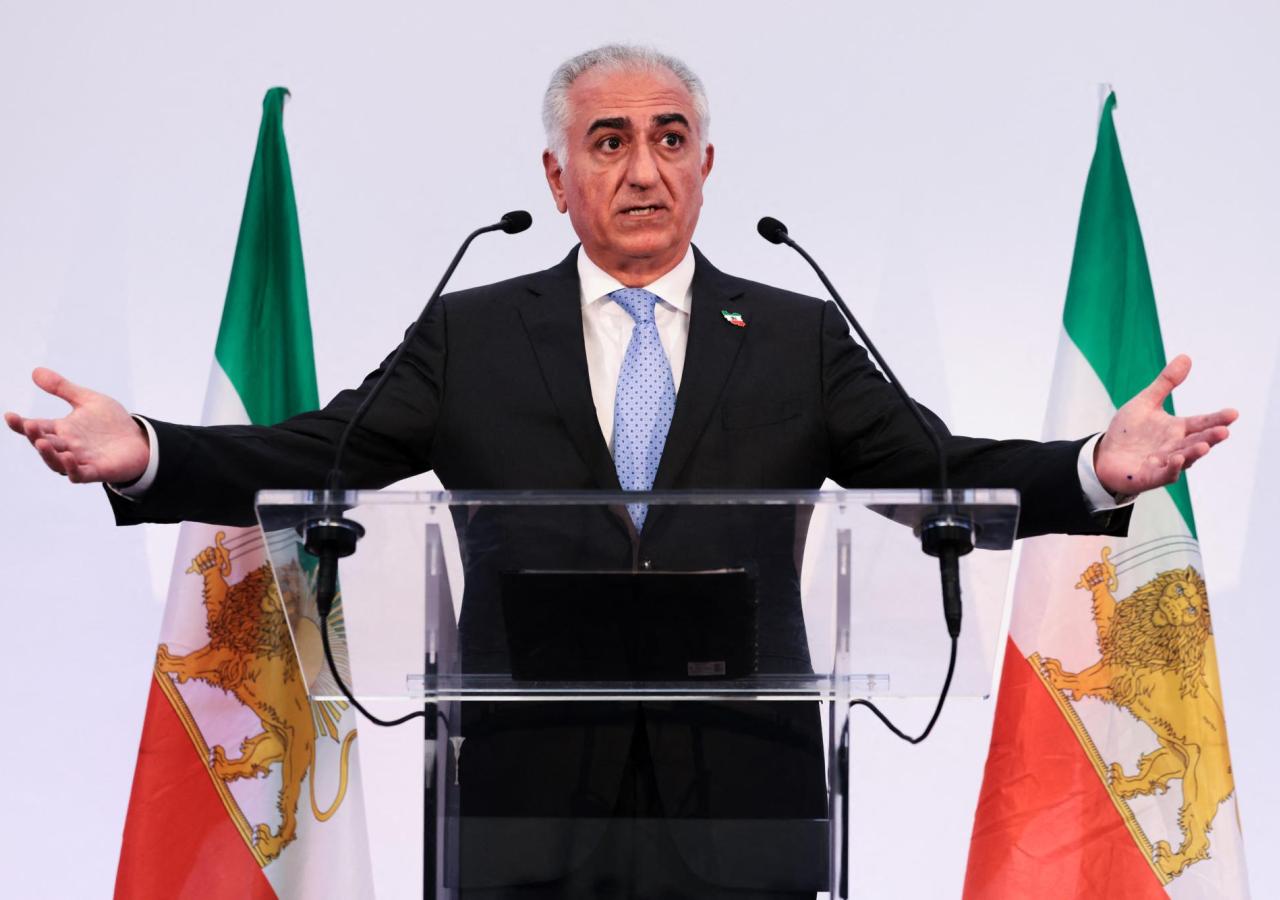 Reza Pahlavi steht vor zwei Iran-Flaggen mit monarchistischen Löwen darauf.