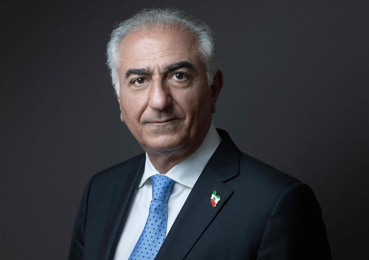 Reza Pahlavi in Anzug vor schwarzem Hintergrund. Man sieht einen kleinen Iran-Pin.